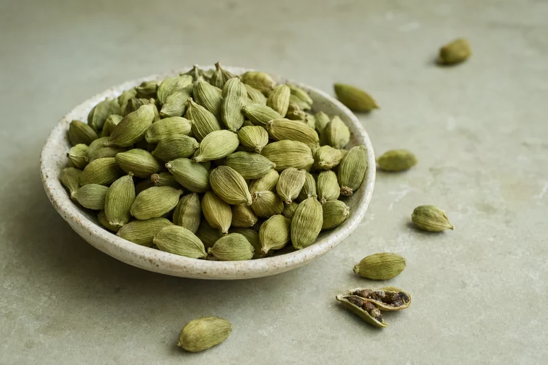 Green cardamom in a ceramic bowl; illustrative product image
